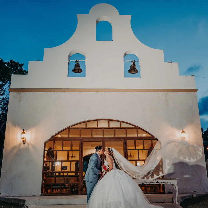 Newlyweds kissing outside a hacienda chapel at dusk